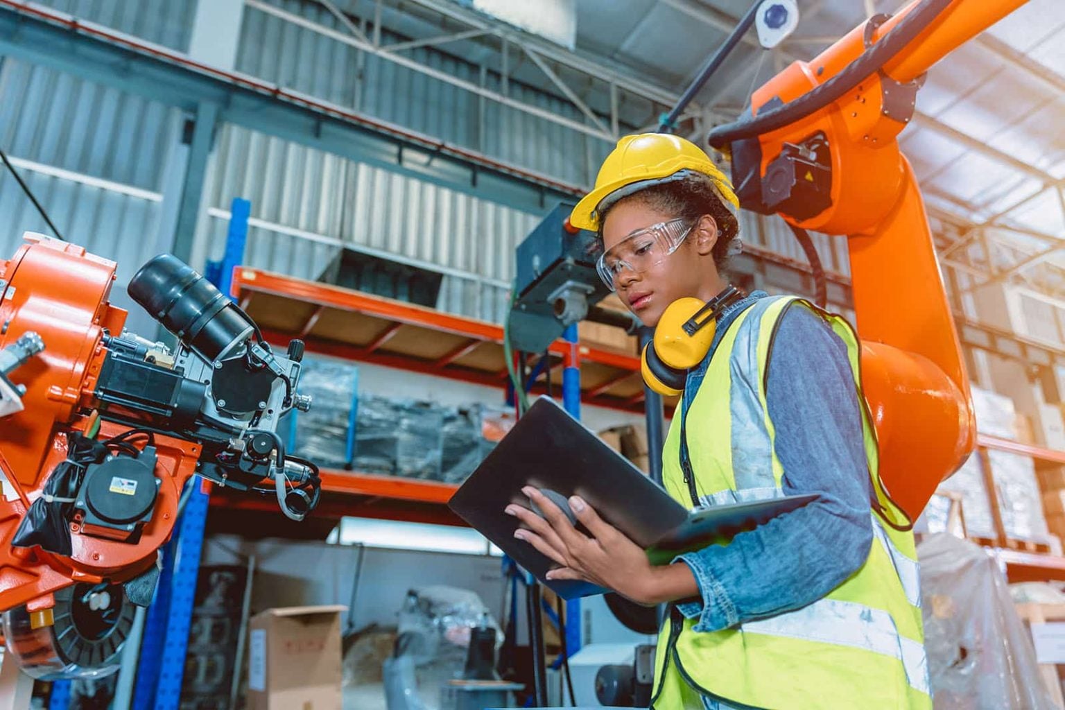 A technician in a hard hat checking a tablet beside a robotic arm