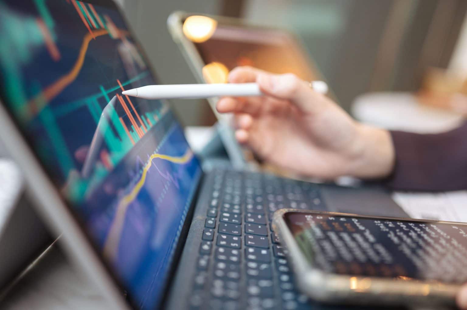 A hand with a stylus over a laptop showing a chart