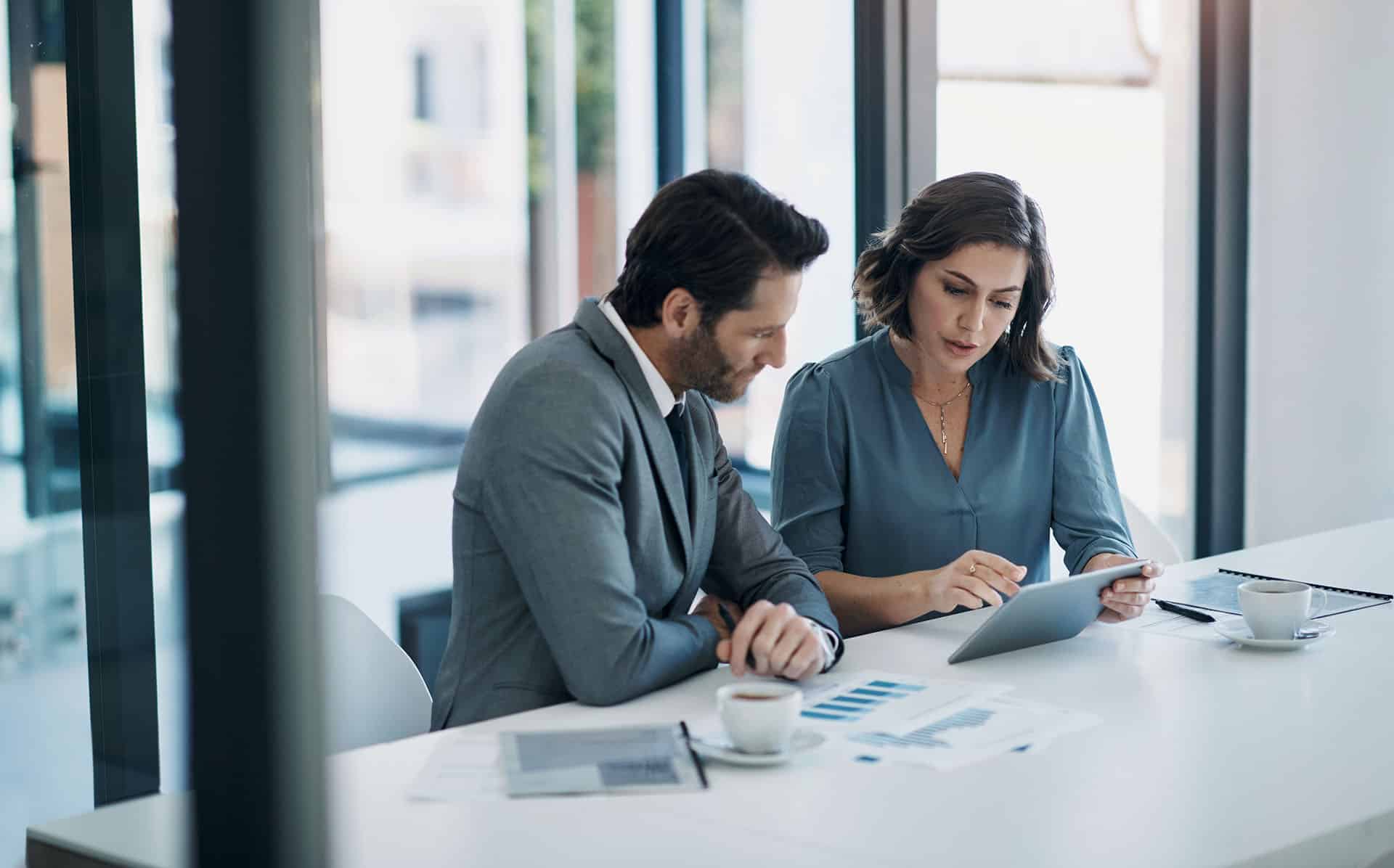 Two colleagues reviewing reports and a tablet at a table