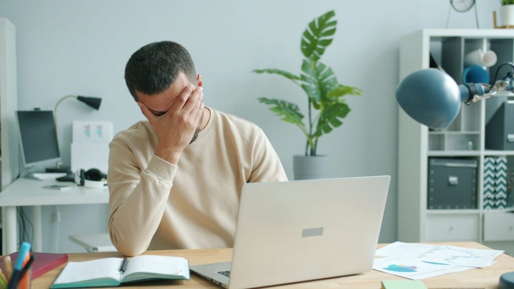 Man rubbing his face in front of a laptop