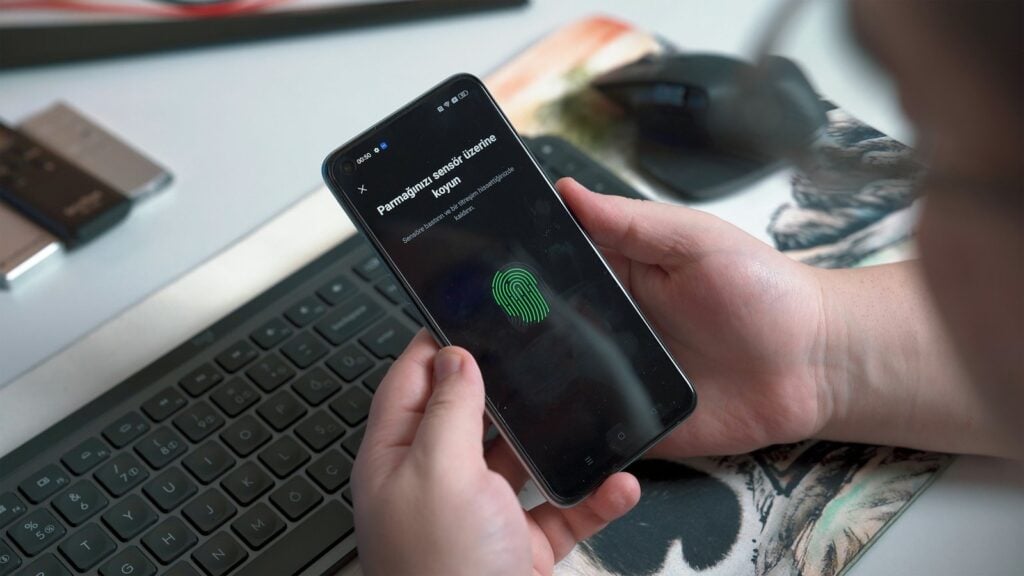 Person approving a sign in with a fingerprint on a phone beside a keyboard
