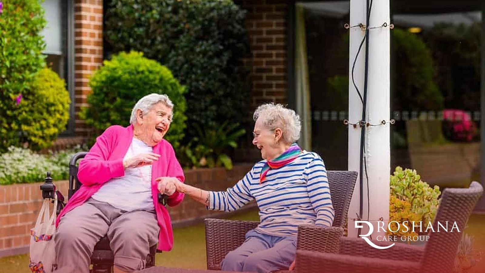 Two Roshana Care Group residents laughing together in a garden courtyard